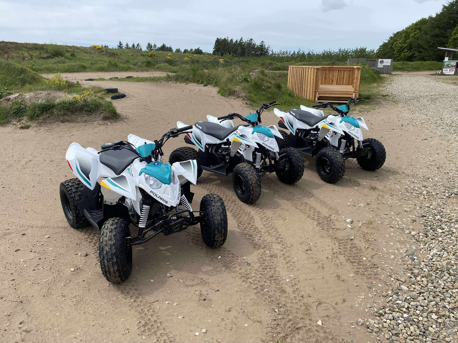 Tre nye hvide og turkise Polaris Outlaw ATV-maskiner opstillet på banen