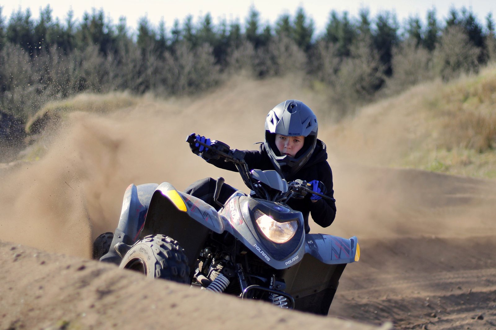 Ung kører tager et skarpt sving på en Polaris ATV i sandet på banen